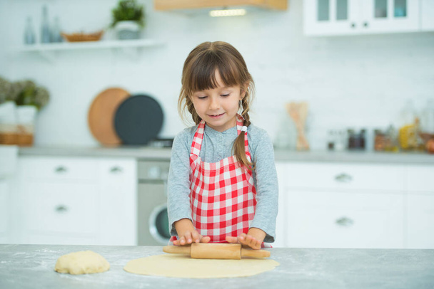A cute little girl with pigtails in a plaid apron kneads pizza dough on her own. Cooking classes for children. - Valokuva, kuva