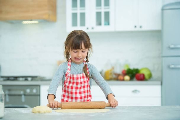 A cute little girl with pigtails in a plaid apron kneads pizza dough on her own. Cooking classes for children. - Foto, immagini
