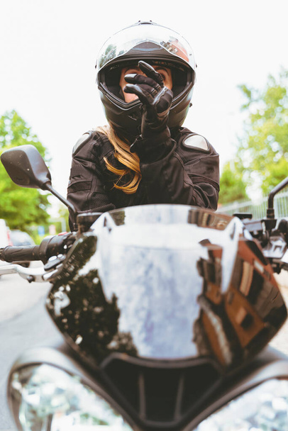 mature woman in motorbiker clothing riding a modern motorcycle outdoors - 写真・画像