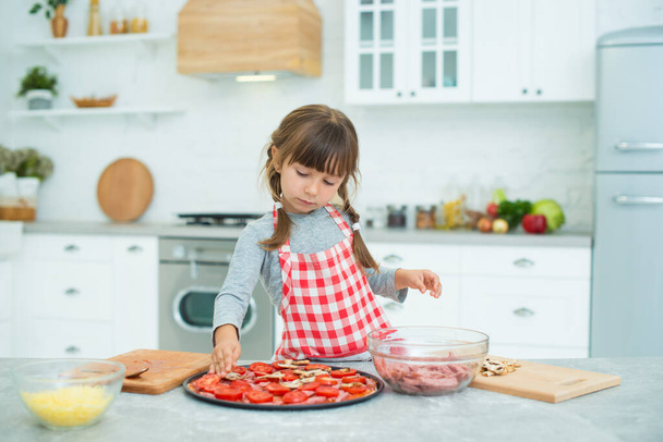 Funny girl with pigtails prepares pizza in the kitchen. Cooking class for children. - Foto, immagini