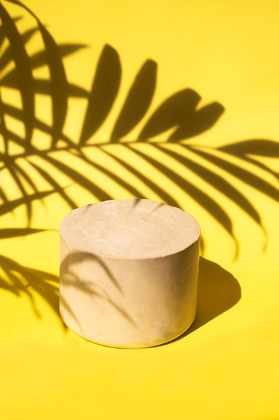 Minimalistic stone podium on yellow background shaded by palm leaves for product display - Valokuva, kuva