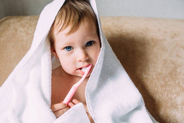 Büyük beyaz havluyla şirin bir çocuk. Onun dişlerini diş fırçasıyla fırçalar.. - Fotoğraf, Görsel