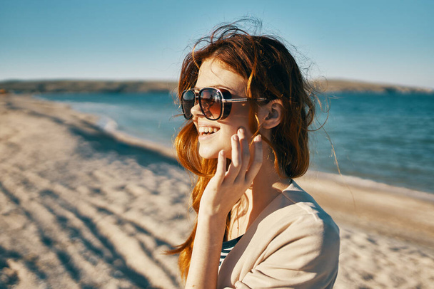 voyageur en veste beige et lunettes de soleil sur le sable près de la mer sur la plage - Photo, image