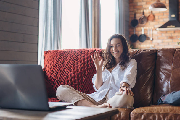 Woman at home waving as she makes video call on laptop computer. - Fotó, kép