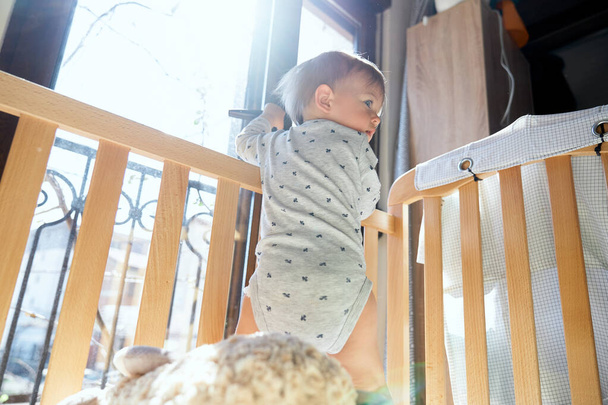 Kid stands in the crib and opens the door to the balcony. Low angle - Photo, Image