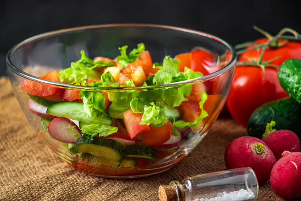 Frischer Gemüsesalat in einer Glasschüssel auf dunklem Hintergrund. Vegane Biolebensmittel, saisonales Sommergericht. - Foto, Bild
