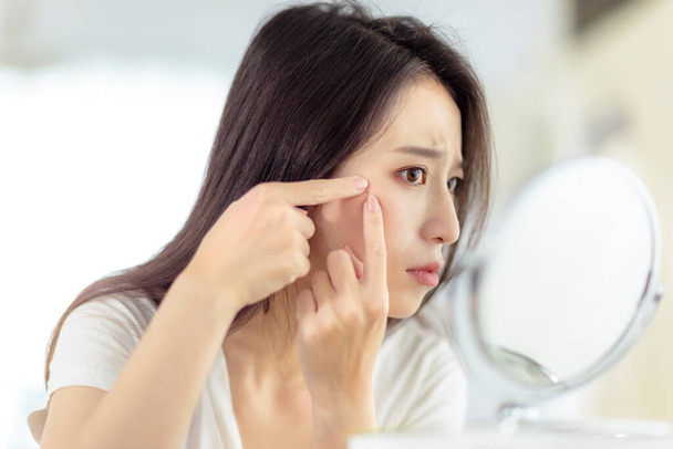 Mujer joven mirando al espejo y comprobando el problema del acné en casa - Foto, imagen