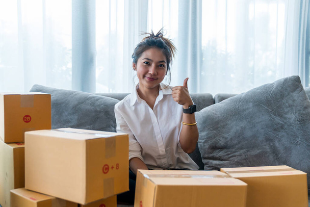 Kauniita aasialaisia naisia, jotka istuvat sohvalla, jossa on monia pakettilaatikoita pienyritysten kanssa, myyvät asiakkaalle verkko-ostoksilla. Konsepti myynti ja ostoksia verkossa kotoa - Valokuva, kuva
