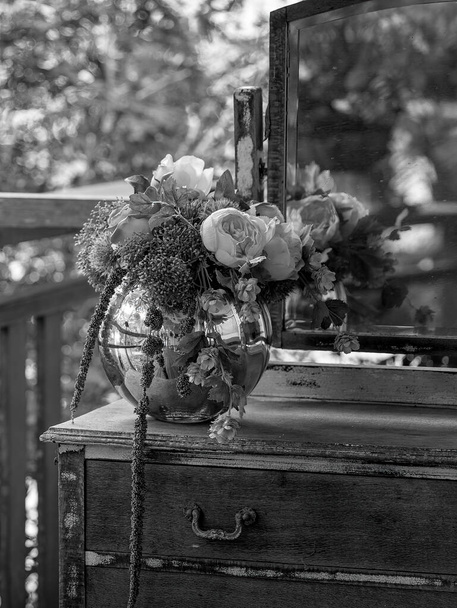 Kolekce starých květin v zrcadlové míčové váze sedící na staré poškrábané příborníku s krásným zahradním světlem, vykreslené v černé a bílé - Fotografie, Obrázek