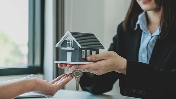 Remettez le modèle de maison à un agent immobilier et expliquez le contrat d'affaires, le loyer, l'achat, l'hypothèque, le prêt ou l'assurance habitation à la femme acheteuse.. - Photo, image