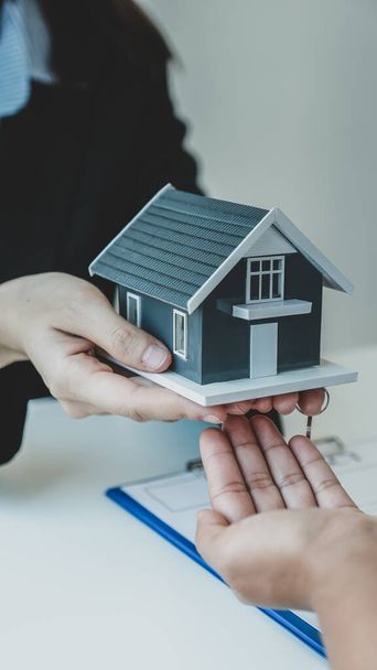 Übergeben Sie einem Immobilienmakler das Hausmodell und erklären Sie der Käuferin den Geschäftsvertrag, die Miete, den Kauf, die Hypothek, den Kredit oder die Hausversicherung.. - Foto, Bild