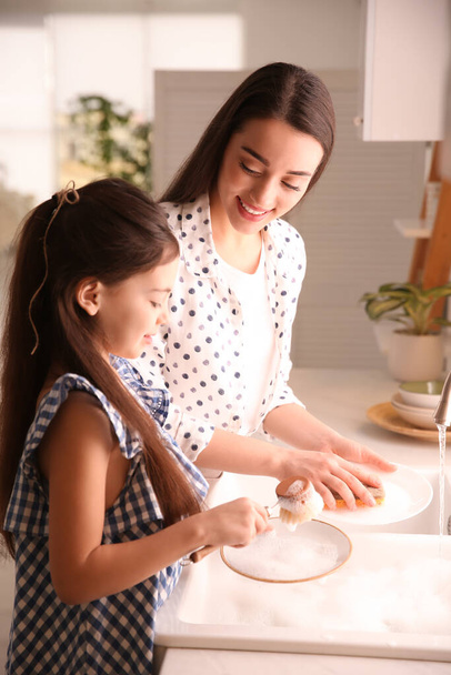 Mother and daughter washing dishes together in kitchen - Foto, imagen