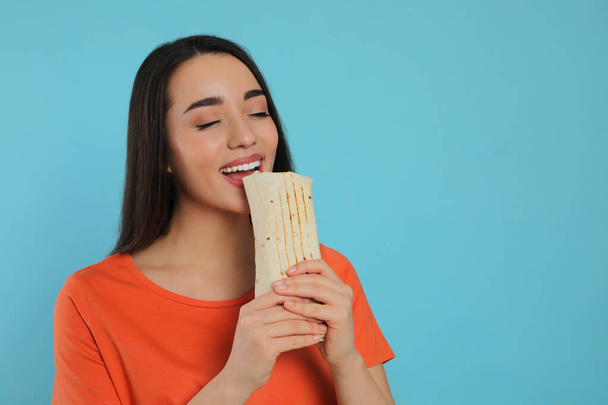 Young woman eating tasty shawarma on turquoise background. Space for text - Fotografie, Obrázek