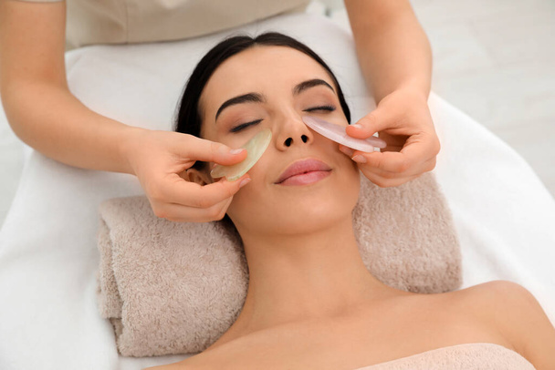 Young woman receiving facial massage with gua sha tools in beauty salon - Zdjęcie, obraz
