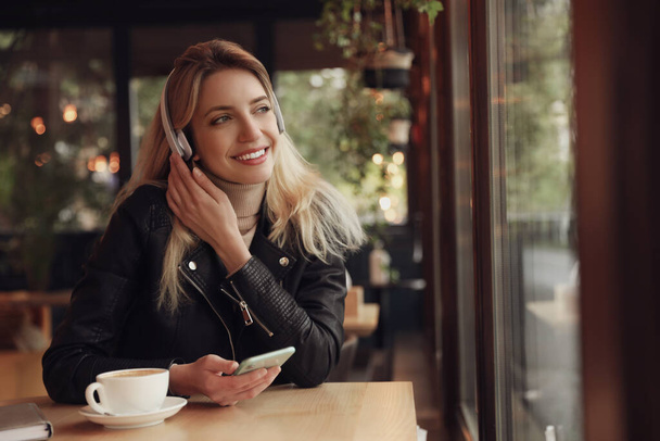 Young woman with headphones and smartphone listening to music in cafe - Photo, image