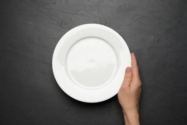 Woman with empty plate at black table, top view - Valokuva, kuva