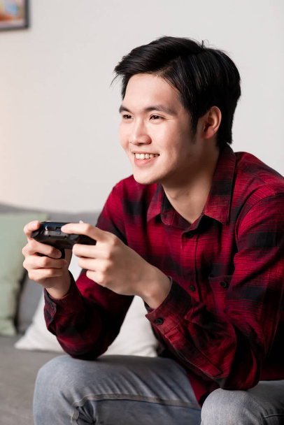 asiatique homme utiliser gamepad et jouer des jeux vidéo heureusement dans la soirée à la maison - Photo, image