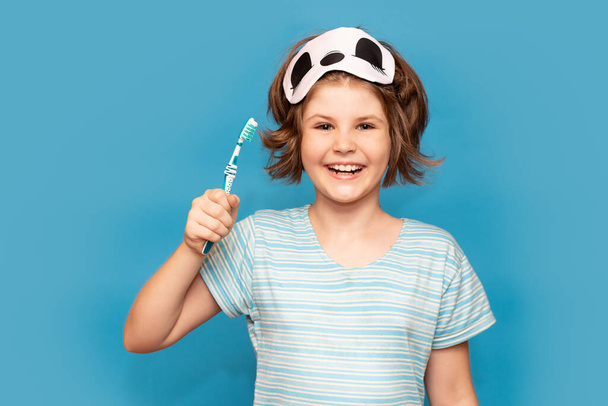 Щаслива дівчинка-дитина зі сплячою маскою чистить зуби зубною щіткою вранці ізольовано на синьому фоні. Охорона здоров'я, гігієна зубів. Макет, місце для копіювання
 - Фото, зображення