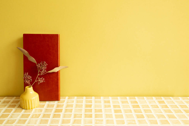 ベージュセラミックモザイクタイルデスク上のドライフラワーのノートと花瓶。黄色い壁の背景。職場・研究所 - 写真・画像