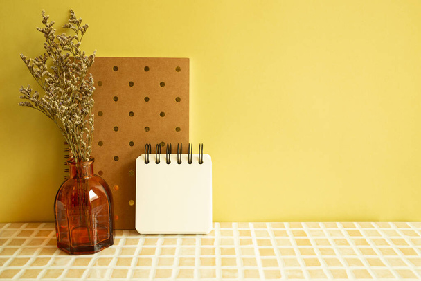 Notebooks and vase of misty blue dry flowers on beige ceramic mosaic tile desk. yellow wall background. Work and study place - Foto, immagini
