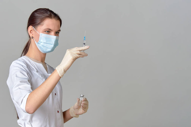 Une infirmière dans un masque médical libère de l'air d'une seringue avec un vaccin, espace de copie - Photo, image