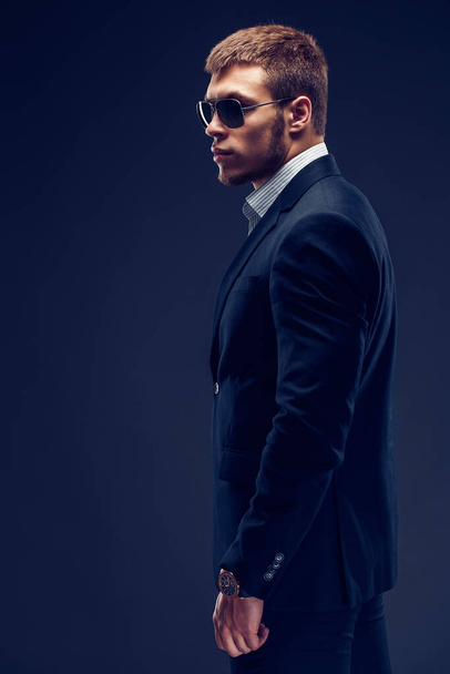 Side view of a Fashion bearded young serious man in sunglasses, luxury suit with one hand in pocket - Valokuva, kuva
