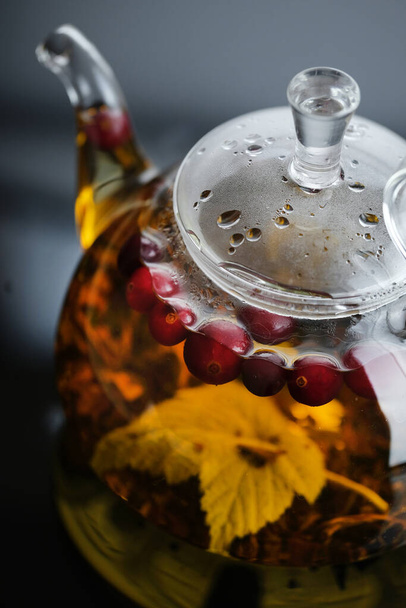 Yellow herbal tea in glass teapot and cup with leaves and berries. Close-up  freshly brewed hot tea. - Foto, afbeelding