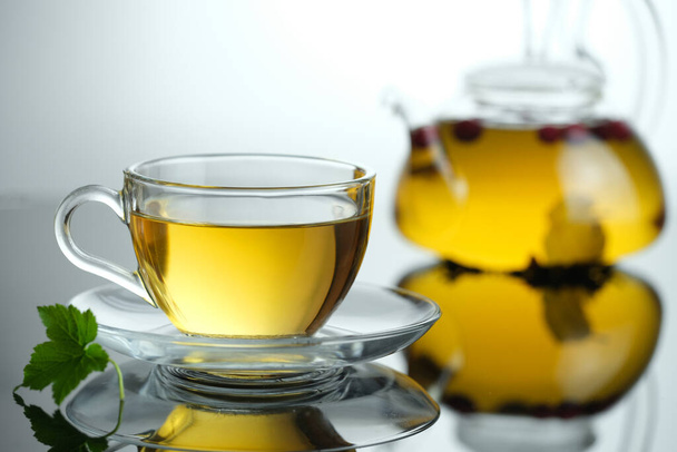 Tisane jaune dans une tasse en verre avec feuille. Gros plan tasse de thé chaud fraîchement infusé. Théière sur fond - Photo, image