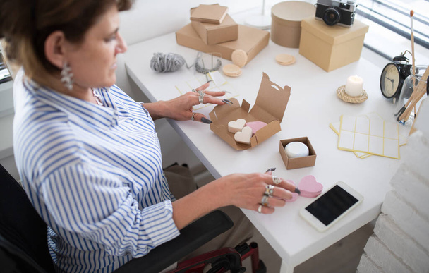 Disabled mature woman in wheelchair packing handmade products indoors at home, small business concept. - Fotografie, Obrázek