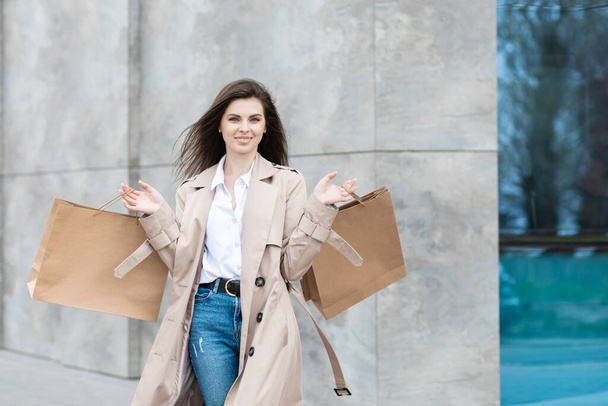 Uma menina em uma roupa casual com sacos de compras e muitas compras perto do centro comercial sorrindo mãos você seu pacote, venda de consumismo e conceito de pessoas. - Foto, Imagem