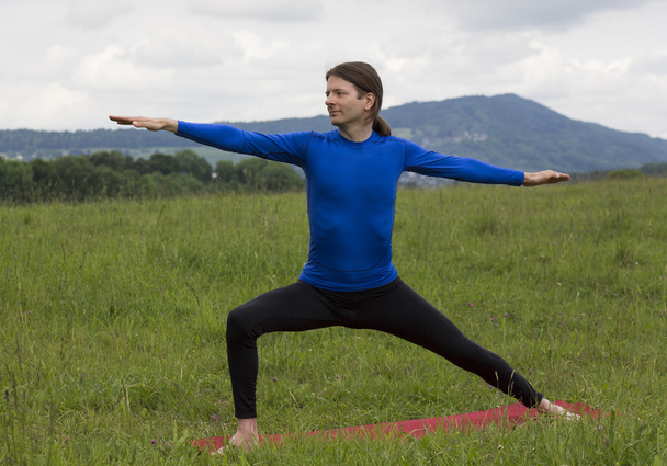 Homem em Guerreiro II Pose durante ioga ao ar livre
 - Foto, Imagem
