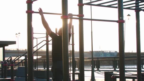 Młody sportowiec trenuje ręce na barach na świeżym powietrzu po zachodzie słońca - Materiał filmowy, wideo