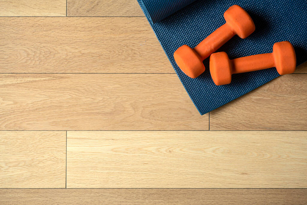 Yoga and fitness background. Wooden floor parquet or laminate with rug and dumbbells for training in a yoga room or gym - Fotó, kép