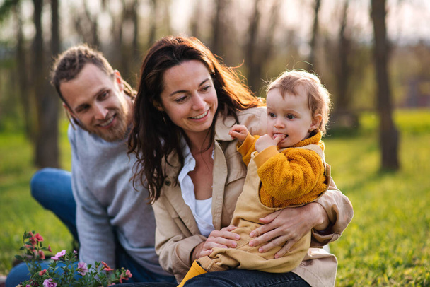 Happy young parents with small baby daughter sitting on grass in nature, relaxing. - Foto, Bild