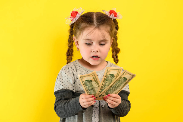 Onnellinen lapsi pitää rahaa, lasten iloa paljon rahaa, muotokuva tytöstä keltaisella taustalla. uusi - Valokuva, kuva