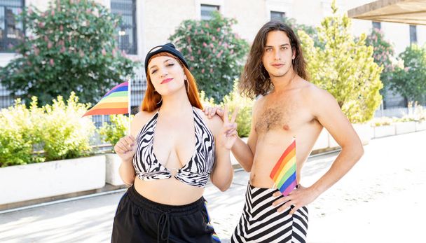 Гей в юбке и лесбиянка в повседневной одежде держат флаги - Фото, изображение
