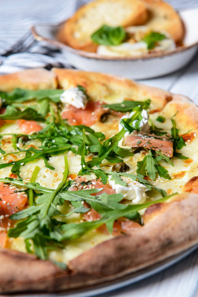 Pizza with mozzarella, salmon slices, fresh arugula. Served with baked cheese camembert and red wine. Italian cuisine concept, traditional pizza recipe. - Fotoğraf, Görsel