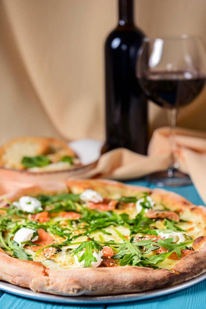 Pizza with mozzarella, salmon slices, fresh arugula. Served with baked cheese camembert and red wine. Italian cuisine concept, traditional pizza recipe. - Photo, Image