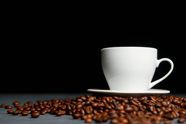 Warm cup of coffee with coffee beans over black background. Coffee time, copy space web design banner. White cup on black background. - Foto, immagini