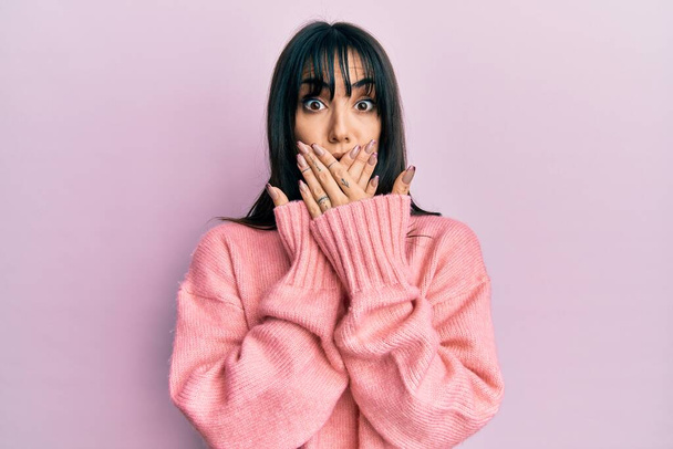 Young brunette woman with bangs wearing casual winter sweater shocked covering mouth with hands for mistake. secret concept.  - Photo, Image