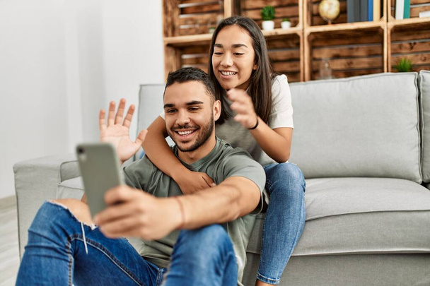 Junges lateinisches Paar lächelt glücklich beim Videoanruf mit Smartphone zu Hause. - Foto, Bild