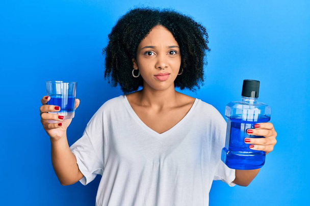 Young african american girl holding mouthwash for fresh breath clueless and confused expression. doubt concept.  - Photo, Image