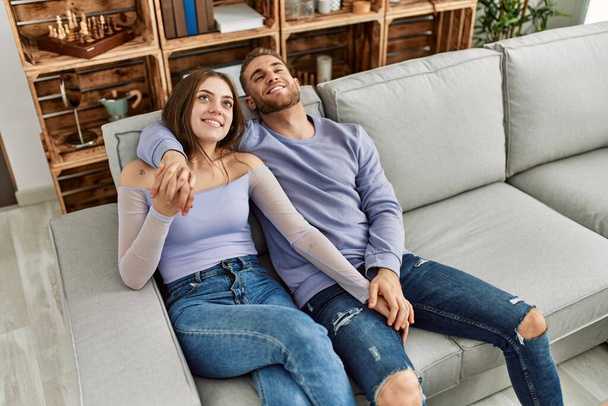 Jovem casal caucasiano relaxado sentado no sofá abraçando em casa. - Foto, Imagem