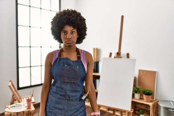 Mujer afroamericana joven con cabello afro en el estudio de arte escéptico y nervioso, frunciendo el ceño molesto debido a un problema. persona negativa.  - Foto, Imagen