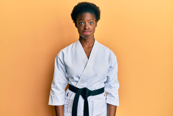 Fiatal afro-amerikai lány karate kimonóval és fekete övvel, vicces arccal. száj felfújt levegővel, őrült kifejezés.  - Fotó, kép
