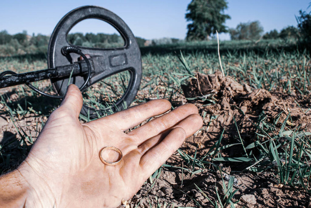 un anillo de oro antiguo en la mano de un buscador, que se encuentra en un antiguo tracto con la ayuda de un detector de metales, el primer plano y el fondo se difuminan con un efecto bokeh - Foto, imagen