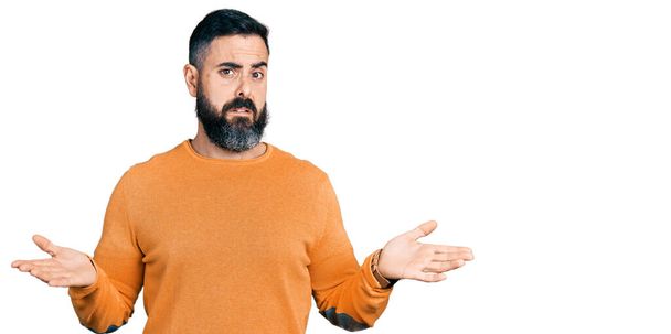 Spanyol férfi szakállal, alkalmi téli pulóvert visel, tanácstalan és összezavarodott nyitott karokkal, fogalma sincs róla..  - Fotó, kép