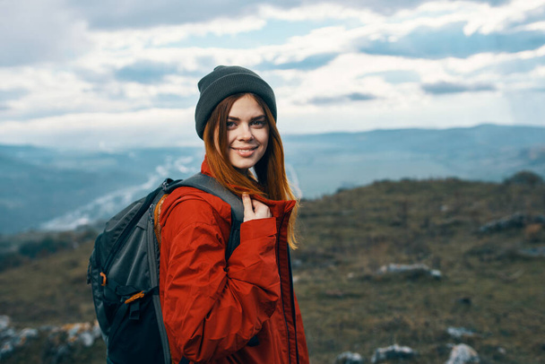 szczęśliwa kobieta w czerwonej kurtce z plecakiem i w górach kapelusza w tle świeże powietrze - Zdjęcie, obraz