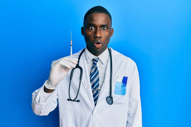 Młody, afrykański lekarz, człowiek trzymający strzykawkę przerażony i zdumiony otwartymi ustami dla zaskoczenia, niedowierzania twarzy  - Zdjęcie, obraz