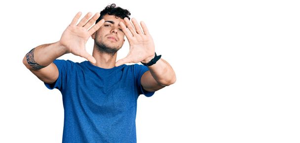 jovem hispânico homem vestindo casual t-shirt fazendo quadro usando mãos palmas e dedos, câmera perspectiva  - Foto, Imagem